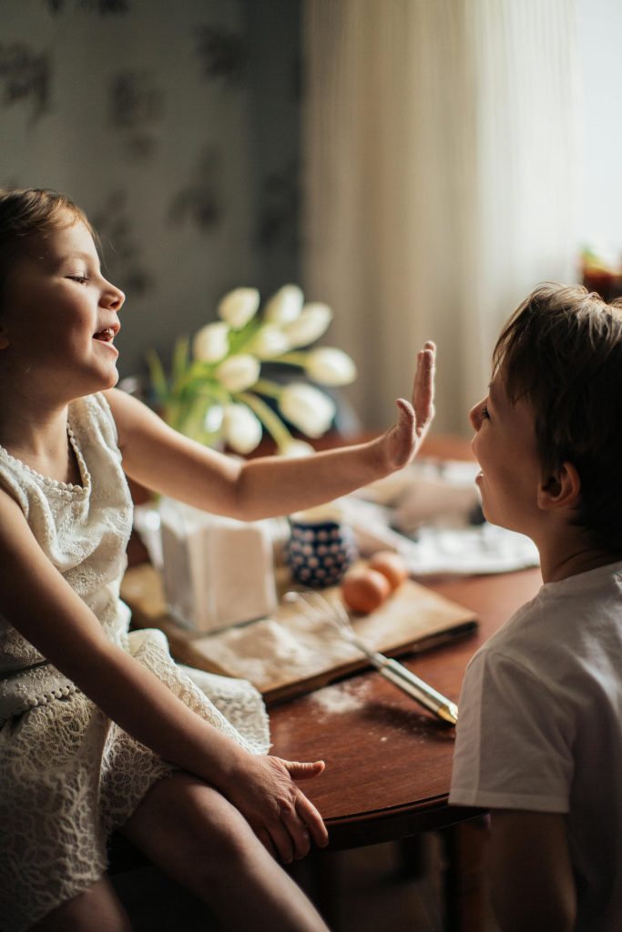 Two siblings laughing and playing while baking indoors, capturing joyful childhood moments.